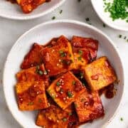 Plate of spicy tofu with chopsticks, sesame, and chives.