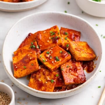 Korean-inspired spicy tofu with chopsticks, sesame, and chives.