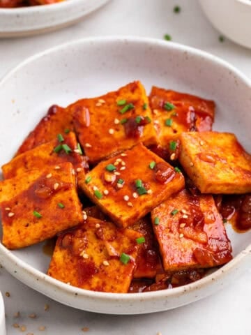 Korean-inspired spicy tofu with chopsticks, sesame, and chives.