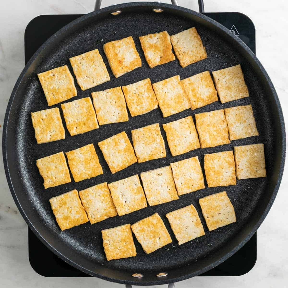 Pan-fried tofu slices in a skillet.