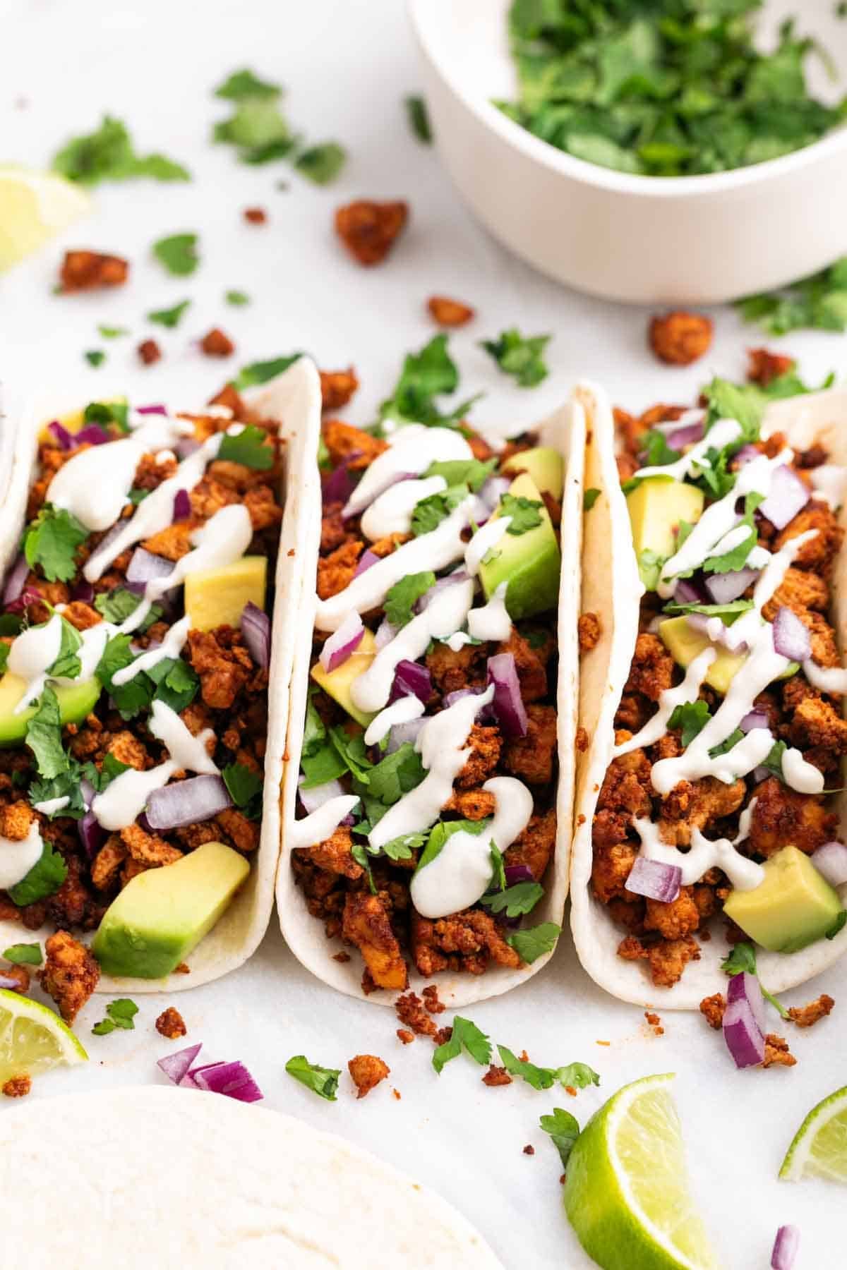 Baked tofu tacos with avocado, red onion, cilantro, and vegan sour cream, with extra toppings on the side.