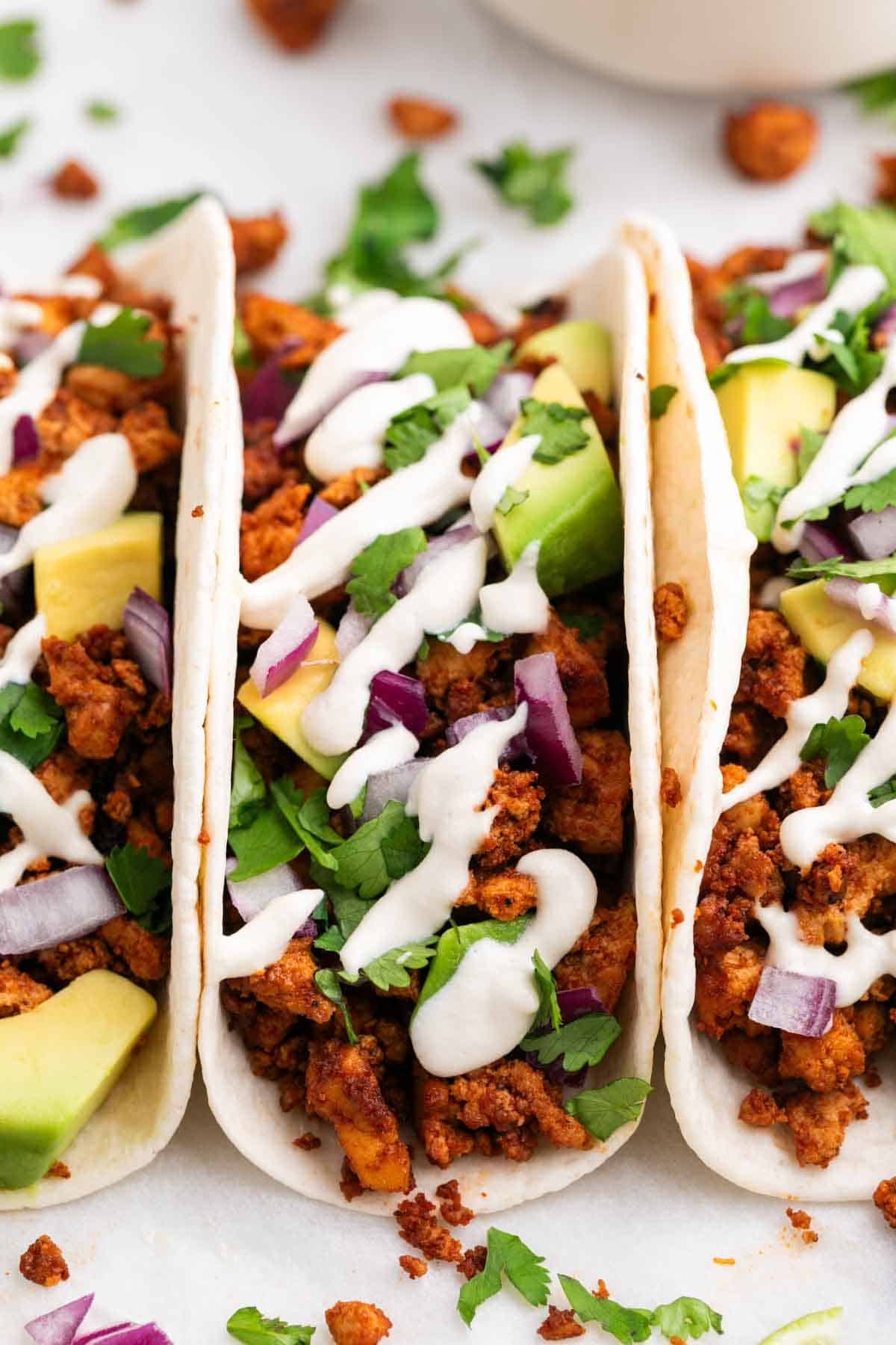 Baked tofu tacos topped with avocado, red onion, cilantro, and vegan sour cream.
