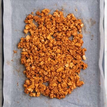 Seasoned tofu crumbles spread in a thin layer on a lined baking sheet.