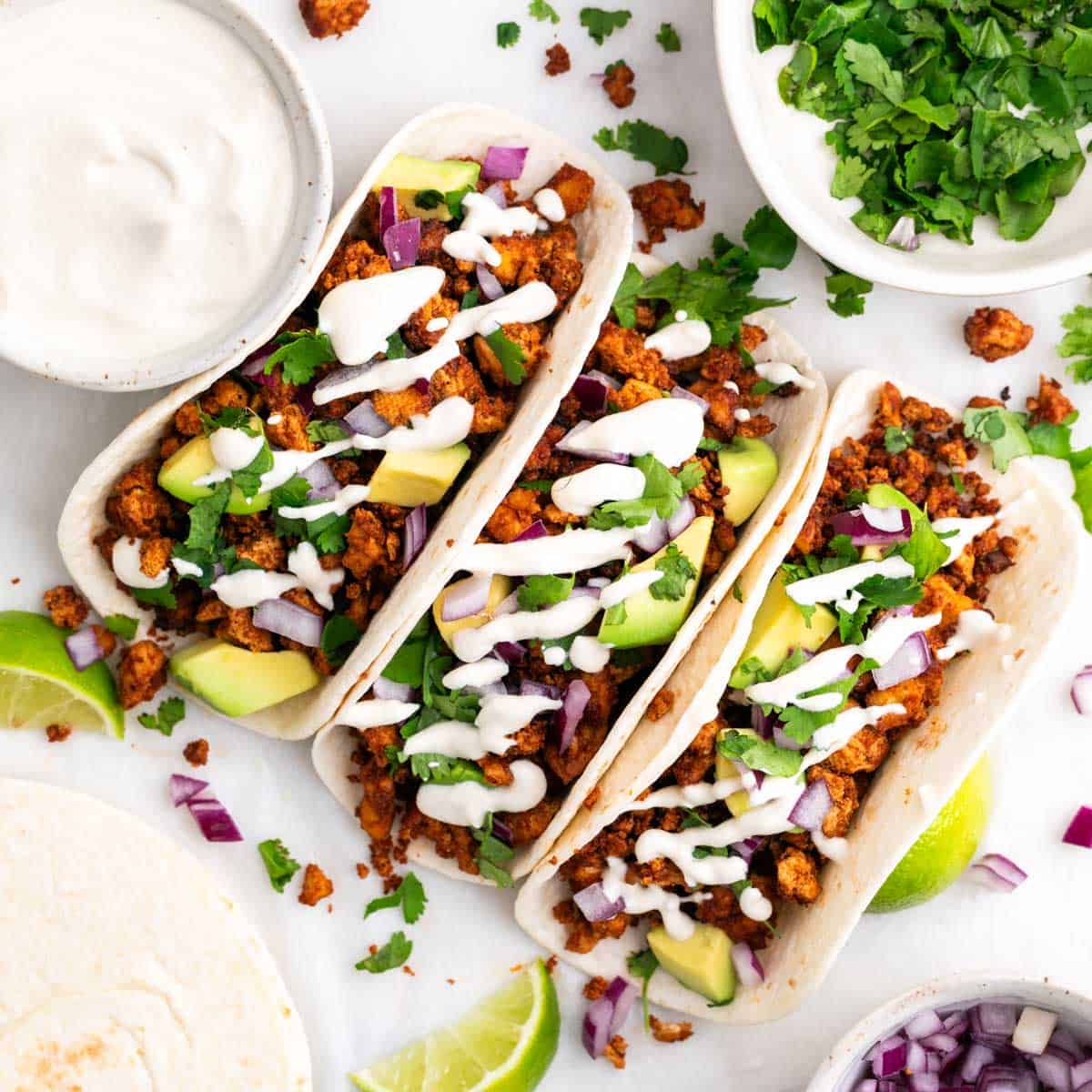 Homemade tofu tacos with avocado, red onion, cilantro, and vegan sour cream, served with extra toppings on the side.