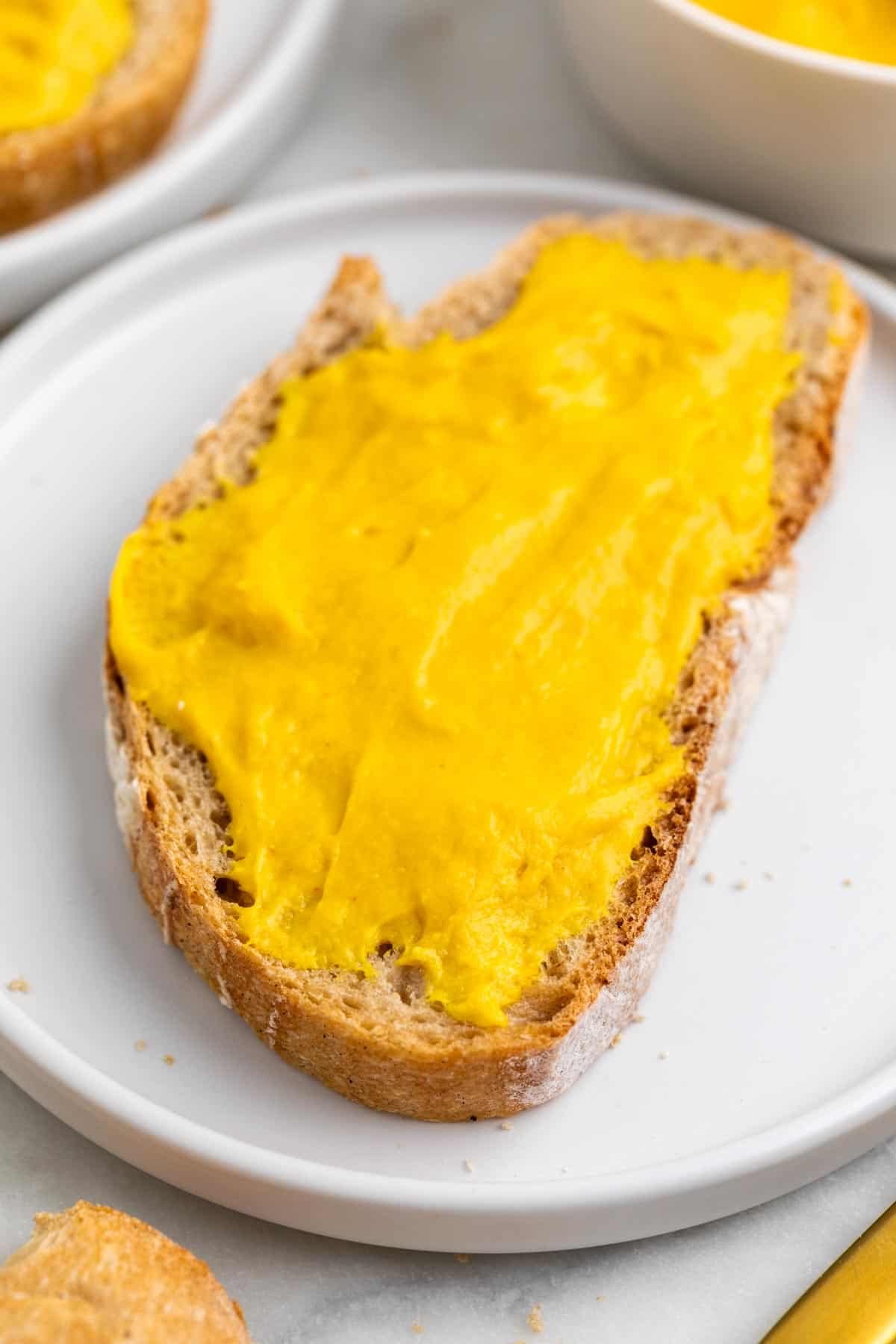 Bread with vegan cheddar cheese spread plated with more bread and a butter knife.