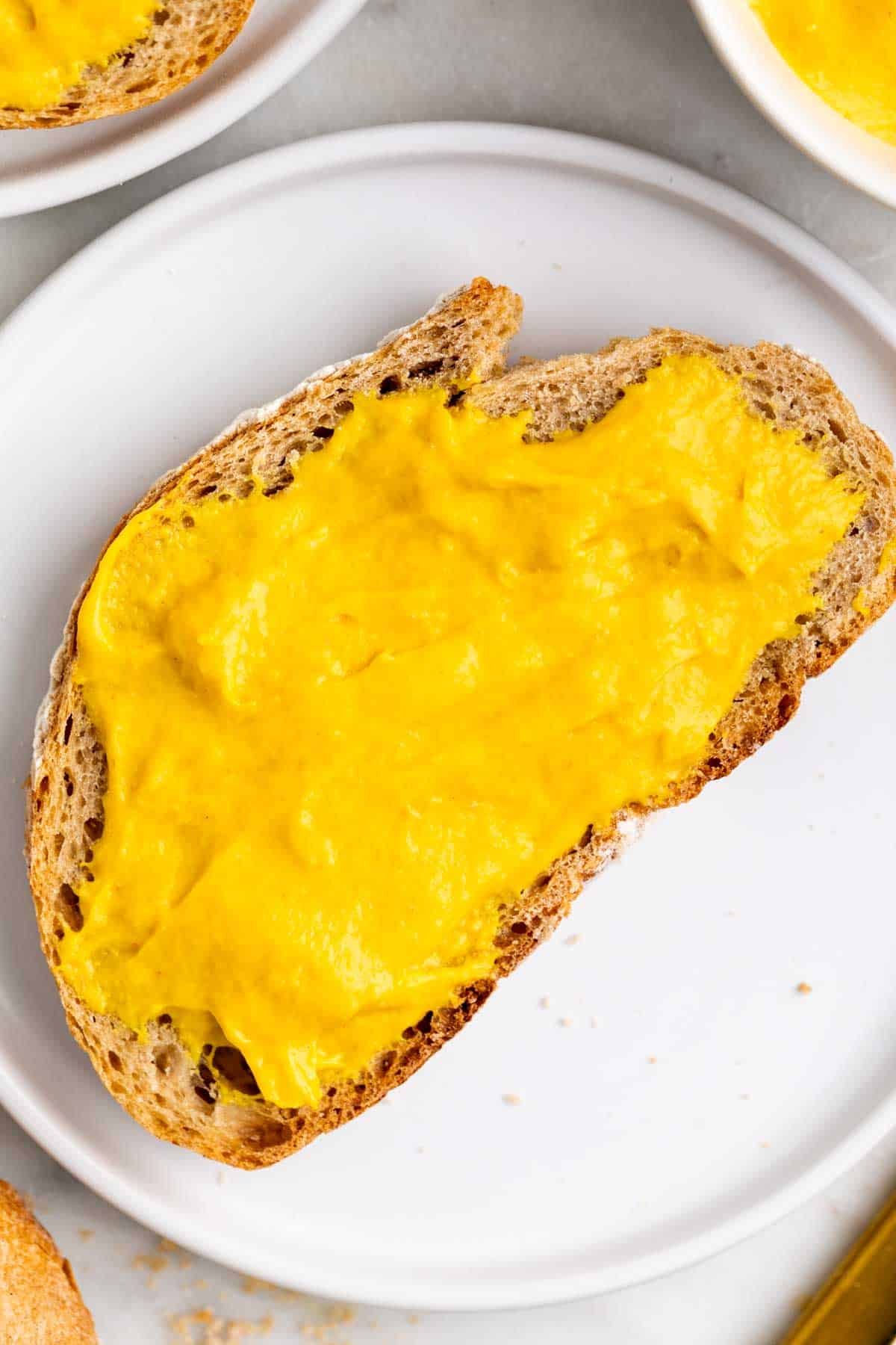 Vegan cheddar cheese spread on a slice of bread served with extra bread and a knife.