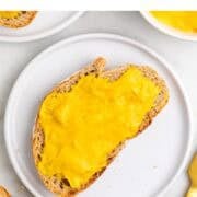 Bread slice with vegan cheddar cheese spread served on a plate with additional slices and a knife.