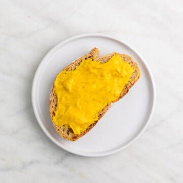 Slice of bread with vegan cheddar cheese spread on a plate.