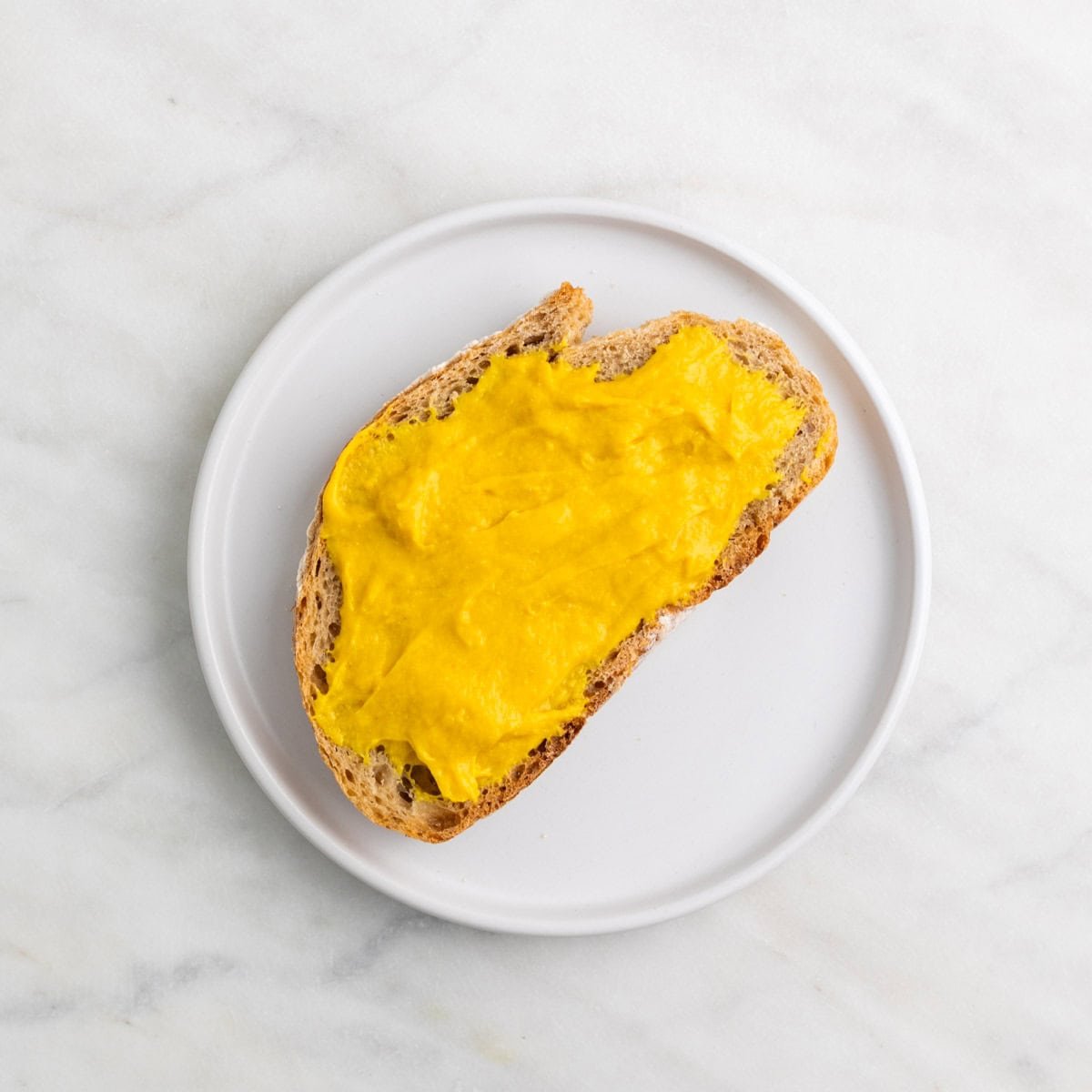 Slice of bread with vegan cheddar cheese spread on a plate.