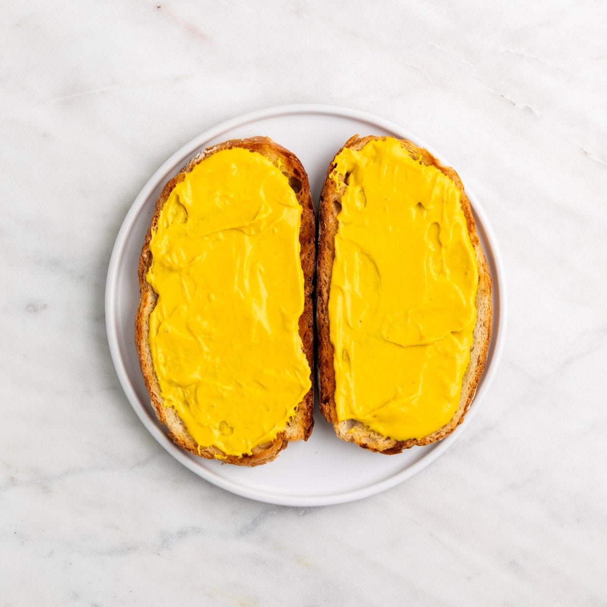 Two slices of bread spread with vegan cheddar cheese spread on a plate.