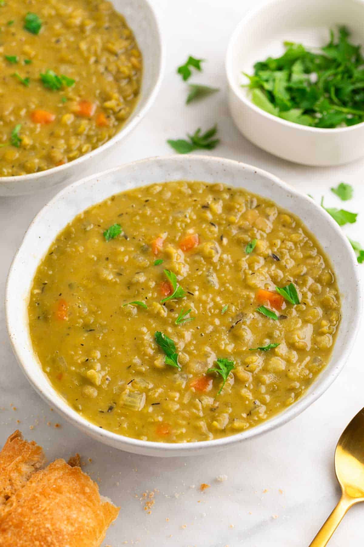 Two bowls of split pea soup with a spoon, bread, and parsley.