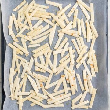 Corn tortilla strips tossed with olive oil on a lined baking sheet before baking.