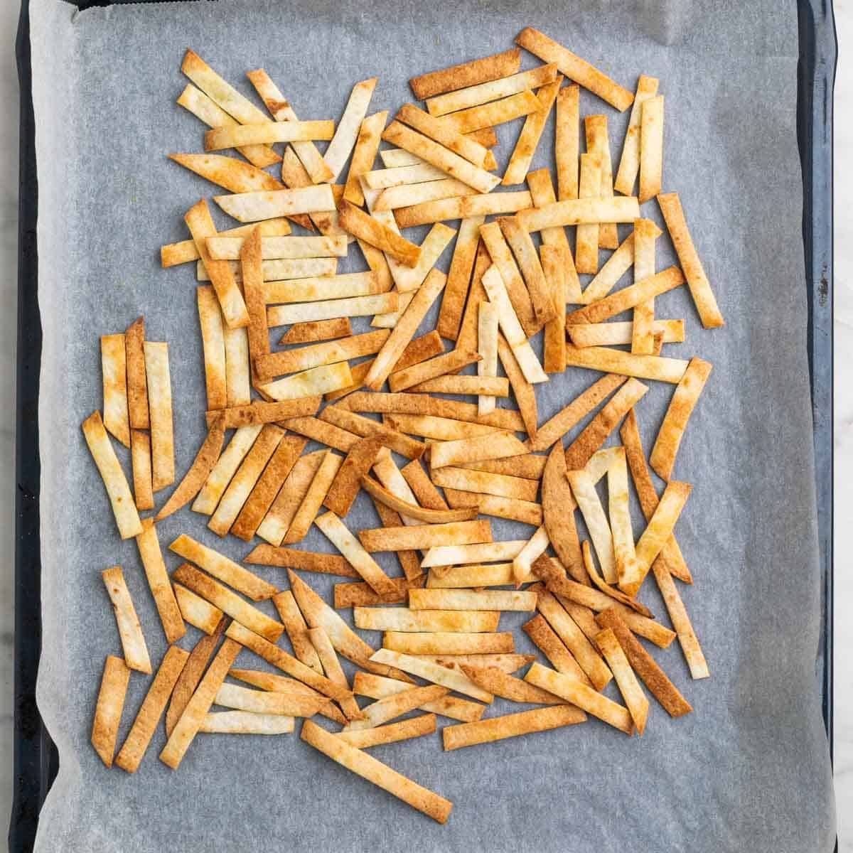 Crispy baked tortilla strips on a baking sheet.