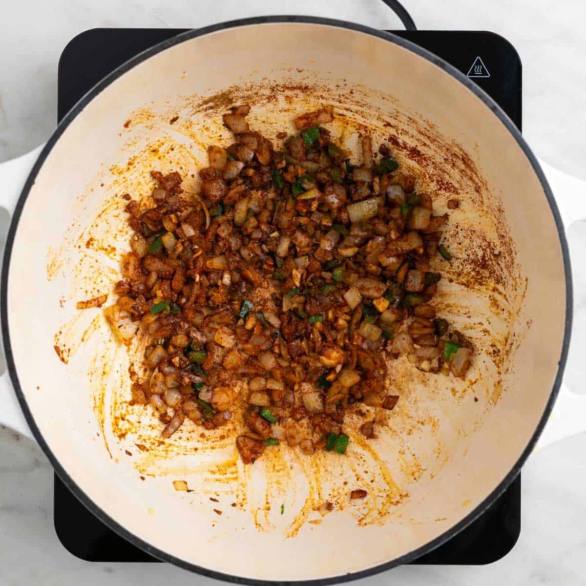 Onion, garlic, jalapeño, and spices cooking together in a pot.