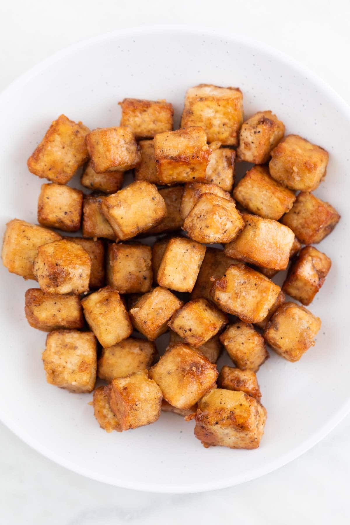 Pan fried tofu with a crispy coating on a white plate.