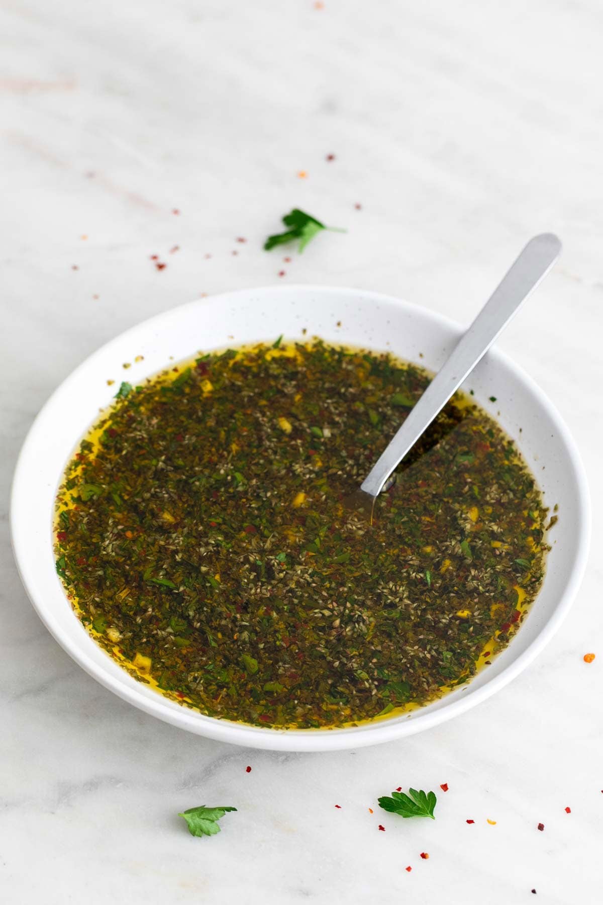 Homemade chimichurri sauce in a bowl with a spoon inside.