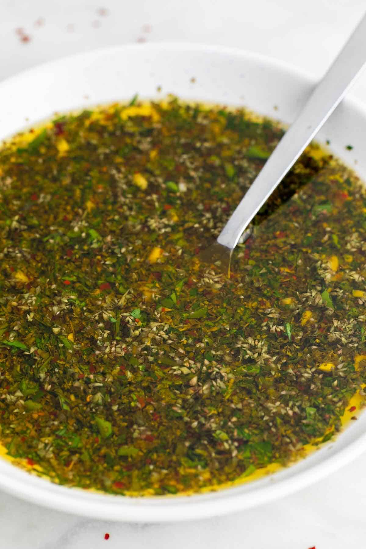 Homemade chimichurri sauce in a bowl with a spoon inside.