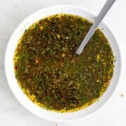 Green chimichurri sauce in a bowl with herbs visible.