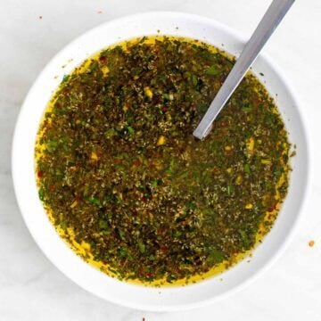 Green chimichurri sauce in a bowl with herbs visible.