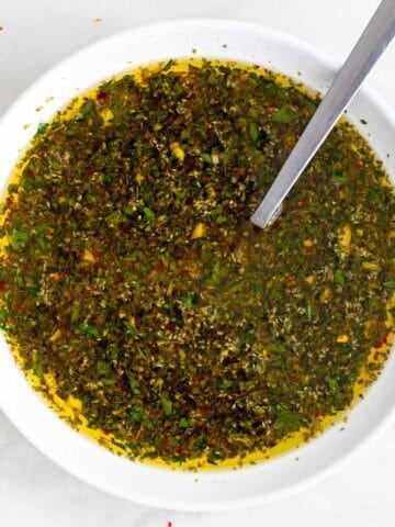 Green chimichurri sauce in a bowl with herbs visible.