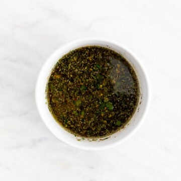 Mixing chimichurri sauce with parsley garlic olive oil and vinegar in a bowl.