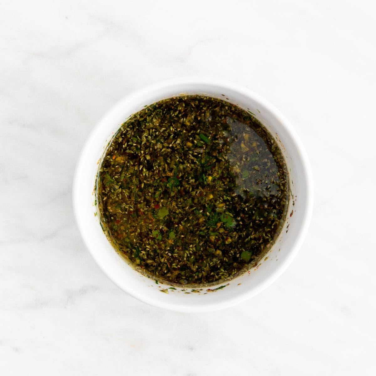 Mixing chimichurri sauce with parsley garlic olive oil and vinegar in a bowl.