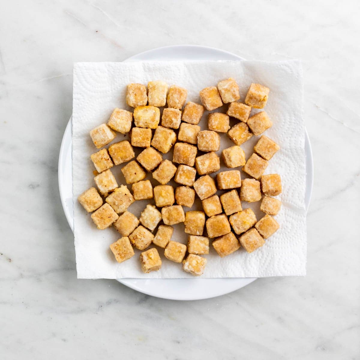 Crispy deep fried tofu on a plate with paper towel.