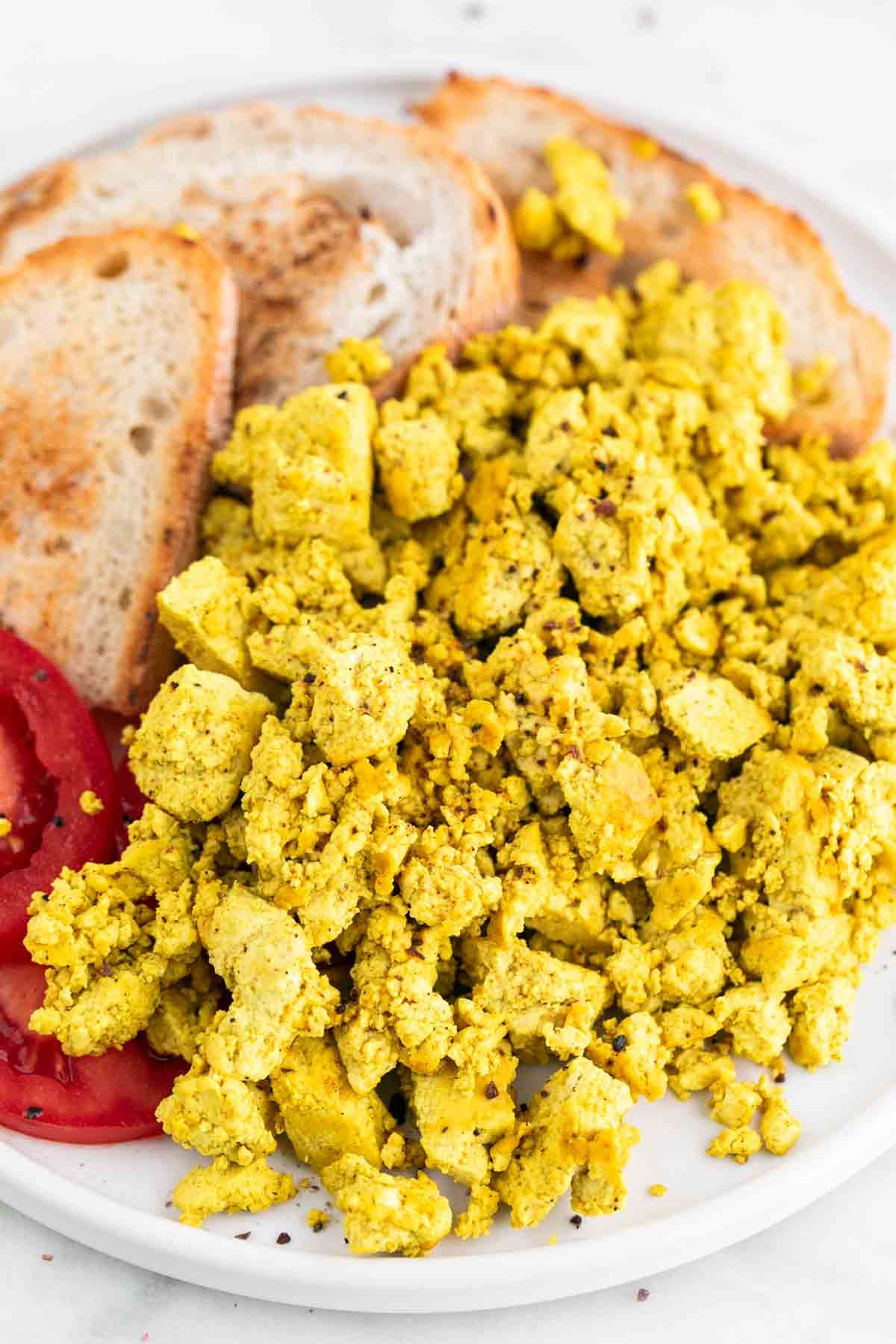 Tofu scramble with bread and tomato slices on a plate.
