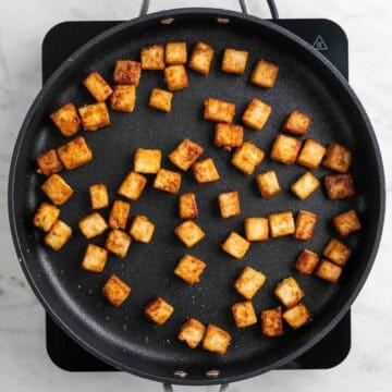 Pan-fried tofu cubes cooking in a skillet.