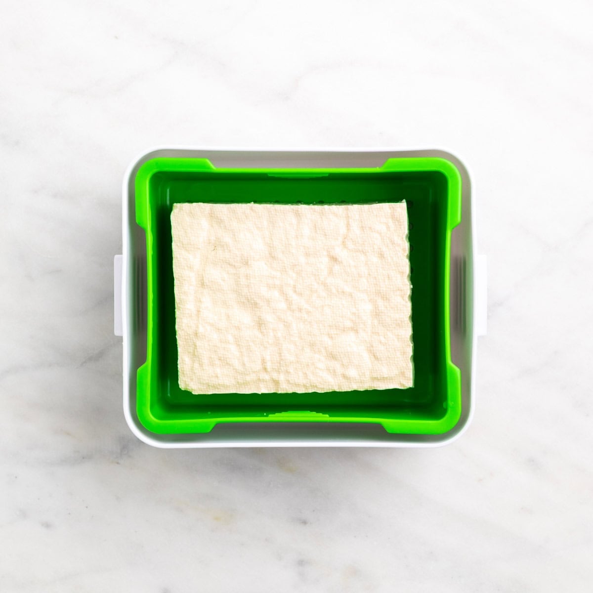 Tofu block inside an open tofu press.