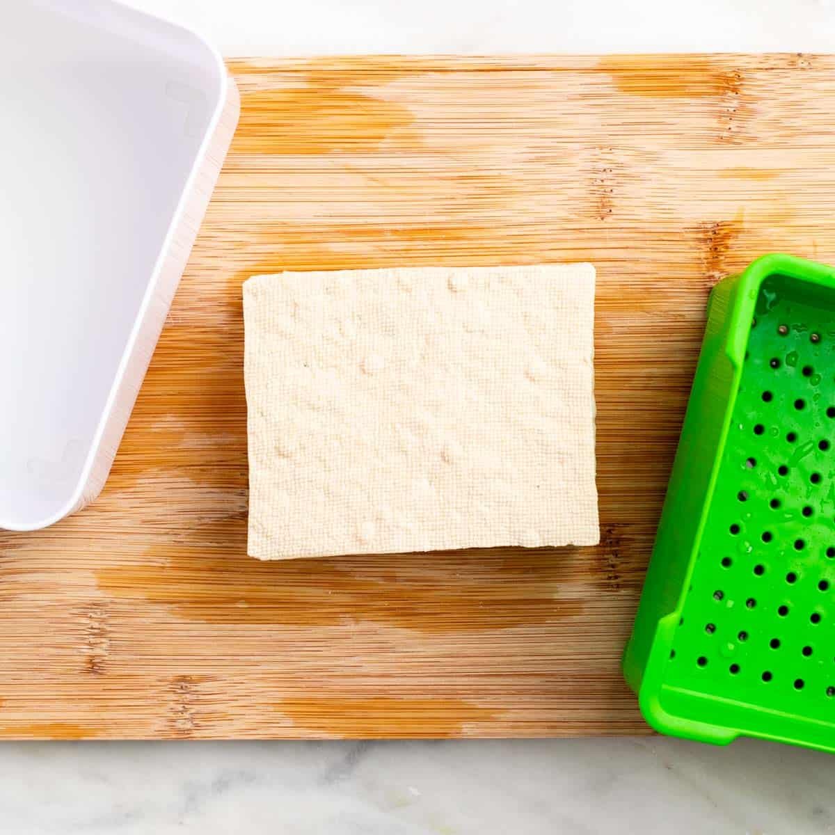 Pressed tofu block next to a tofu press.