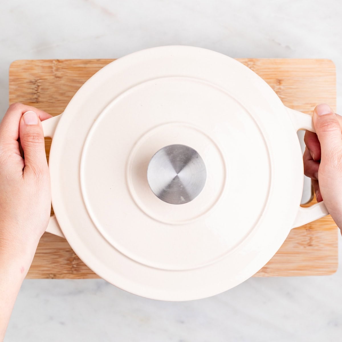 Hands placing a pot on a cutting board to press tofu.