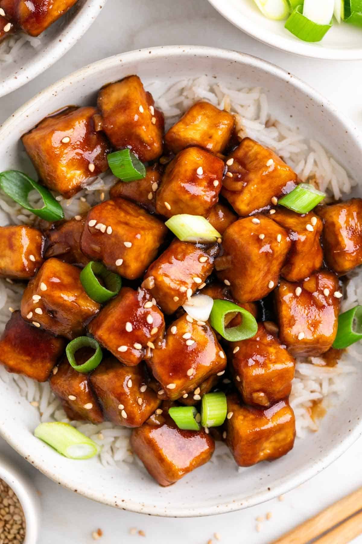 Mongolian tofu bowls with rice, sesame seeds, scallions, and chopsticks.