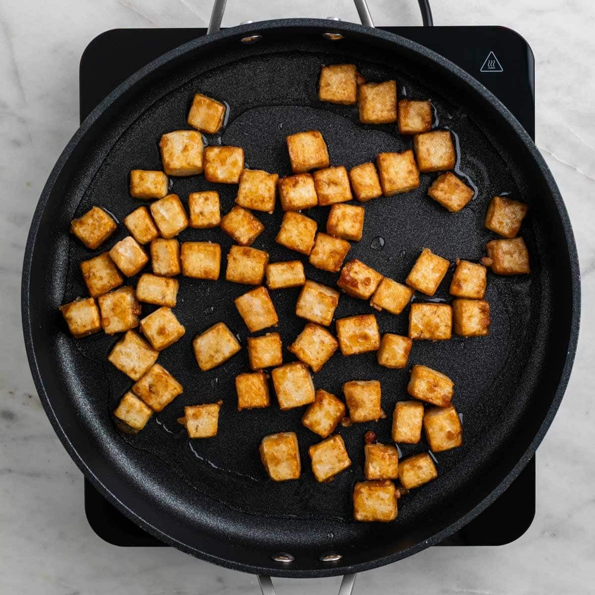 Tofu cooking in a skillet until crispy.