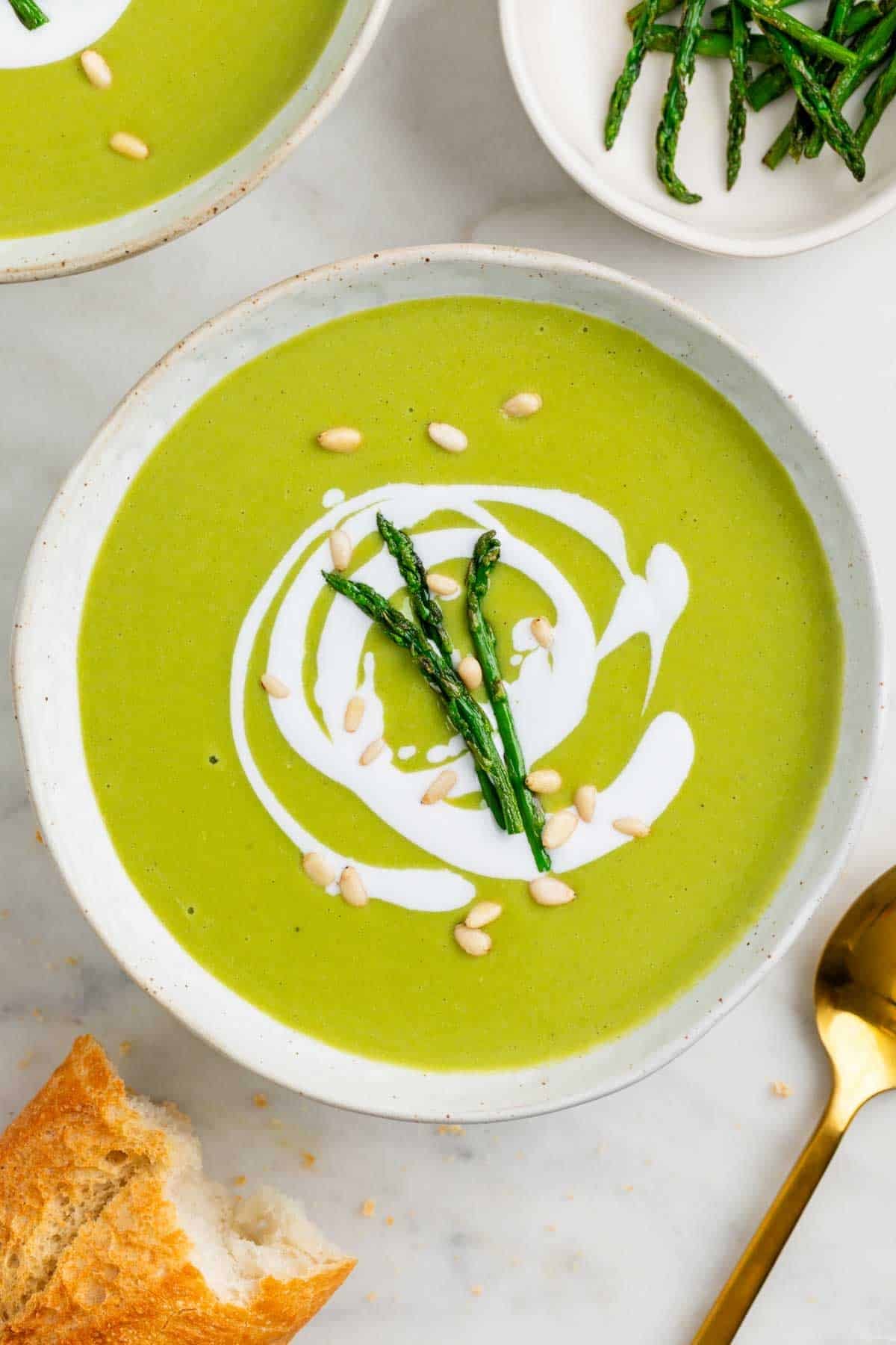 Two bowls of vegan asparagus soup with coconut milk pine nuts and sautéed asparagus.