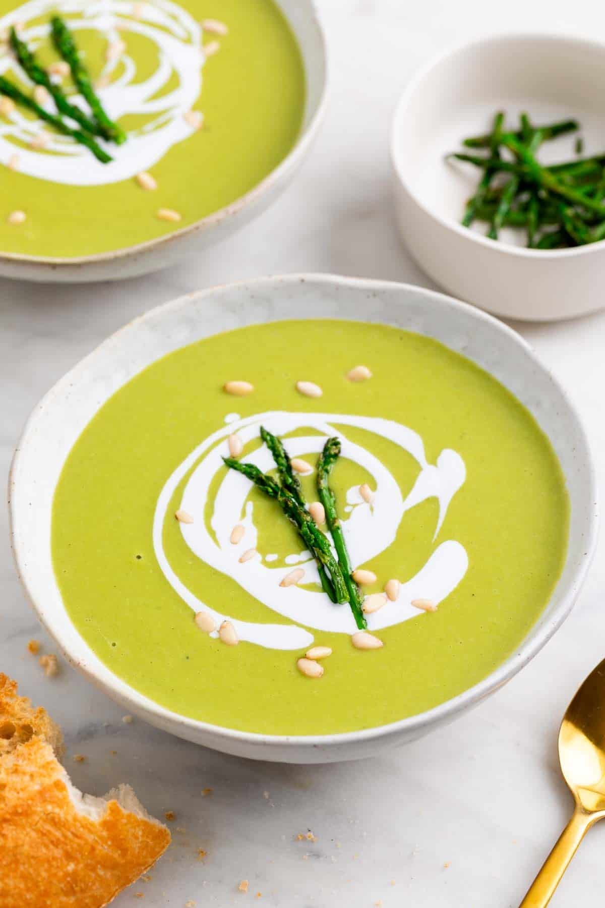 Two bowls of creamy asparagus soup with coconut milk pine nuts and asparagus.