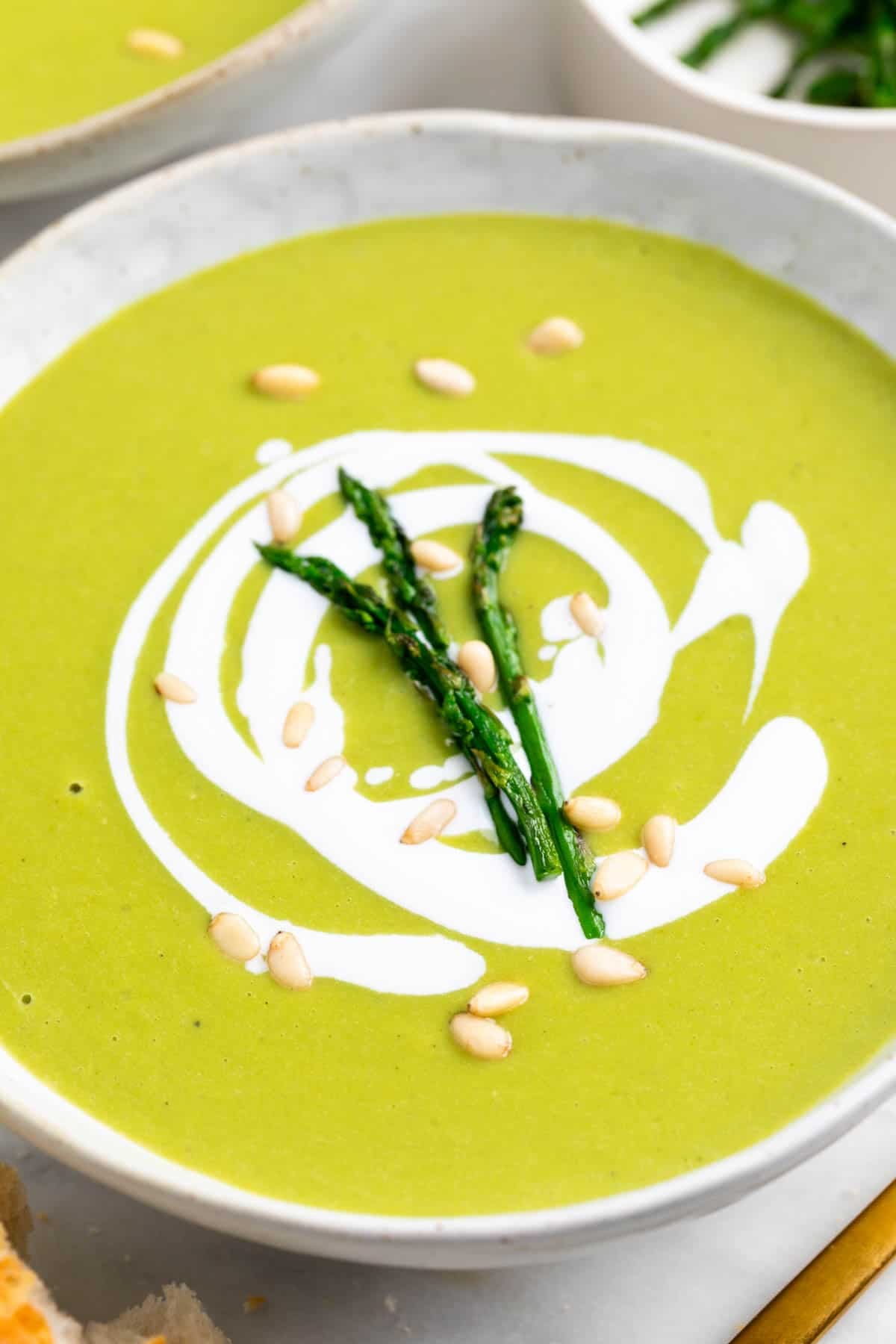 Vegan asparagus soup topped with coconut milk pine nuts and sautéed asparagus.