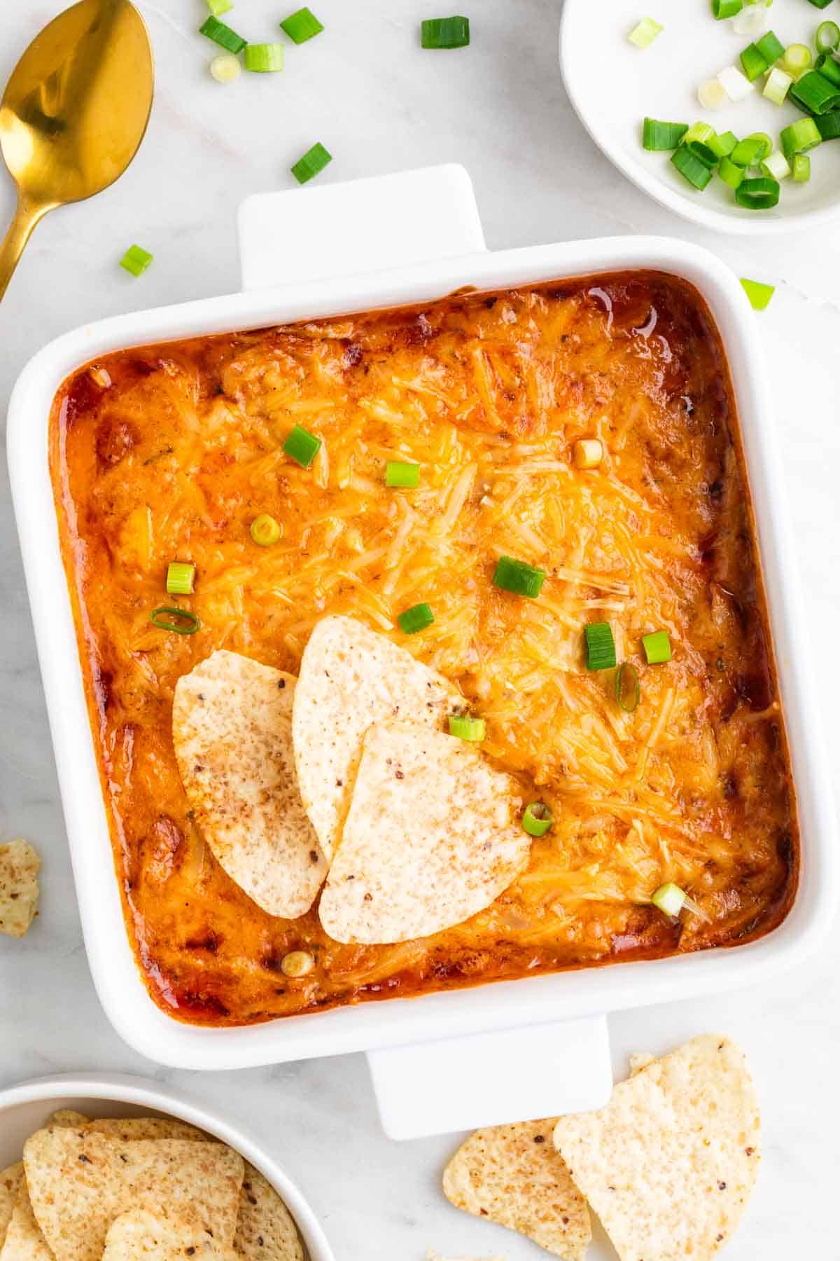 Vegan buffalo chicken dip in a baking dish topped with scallions.