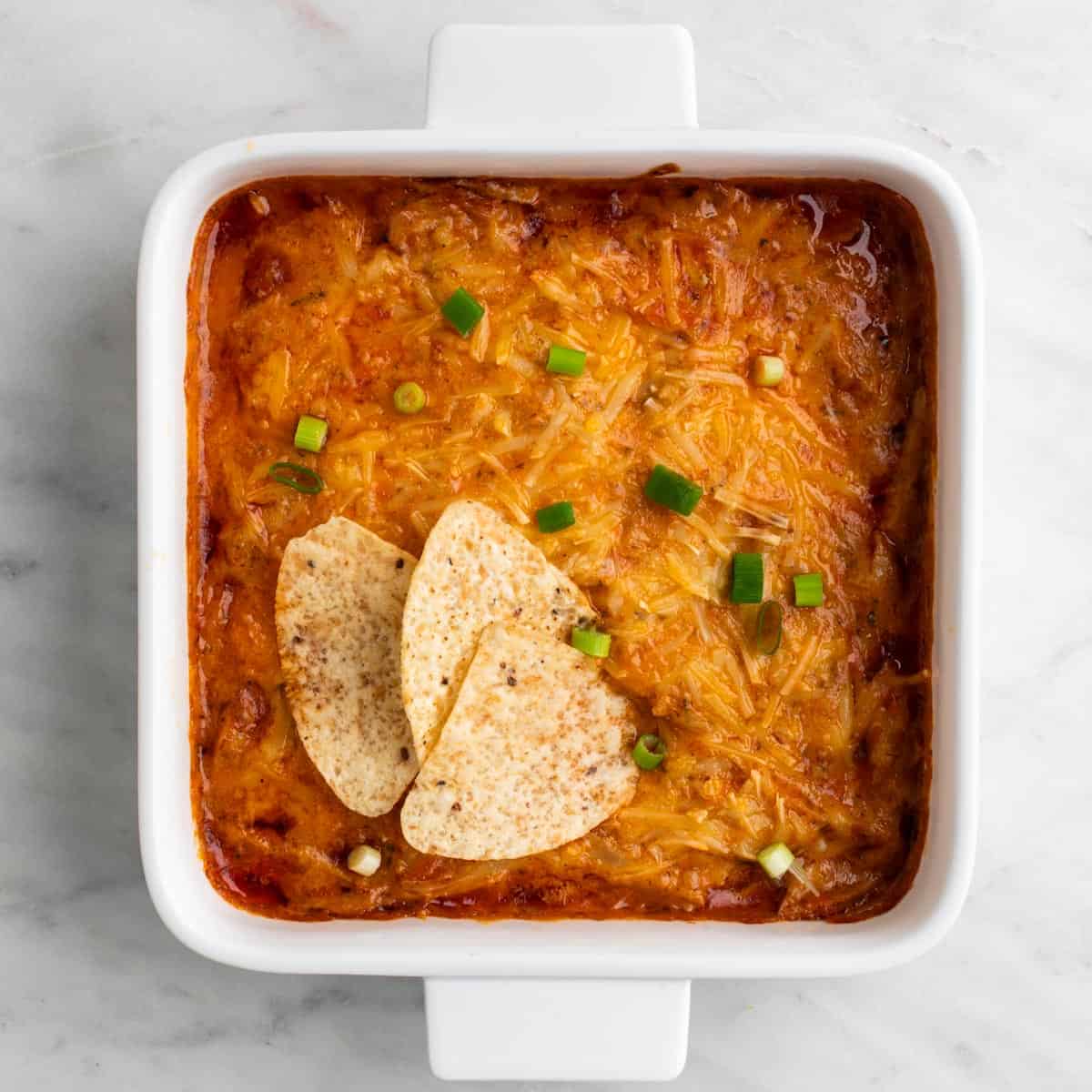 Vegan buffalo chicken dip topped with scallions and served with tortilla chips.
