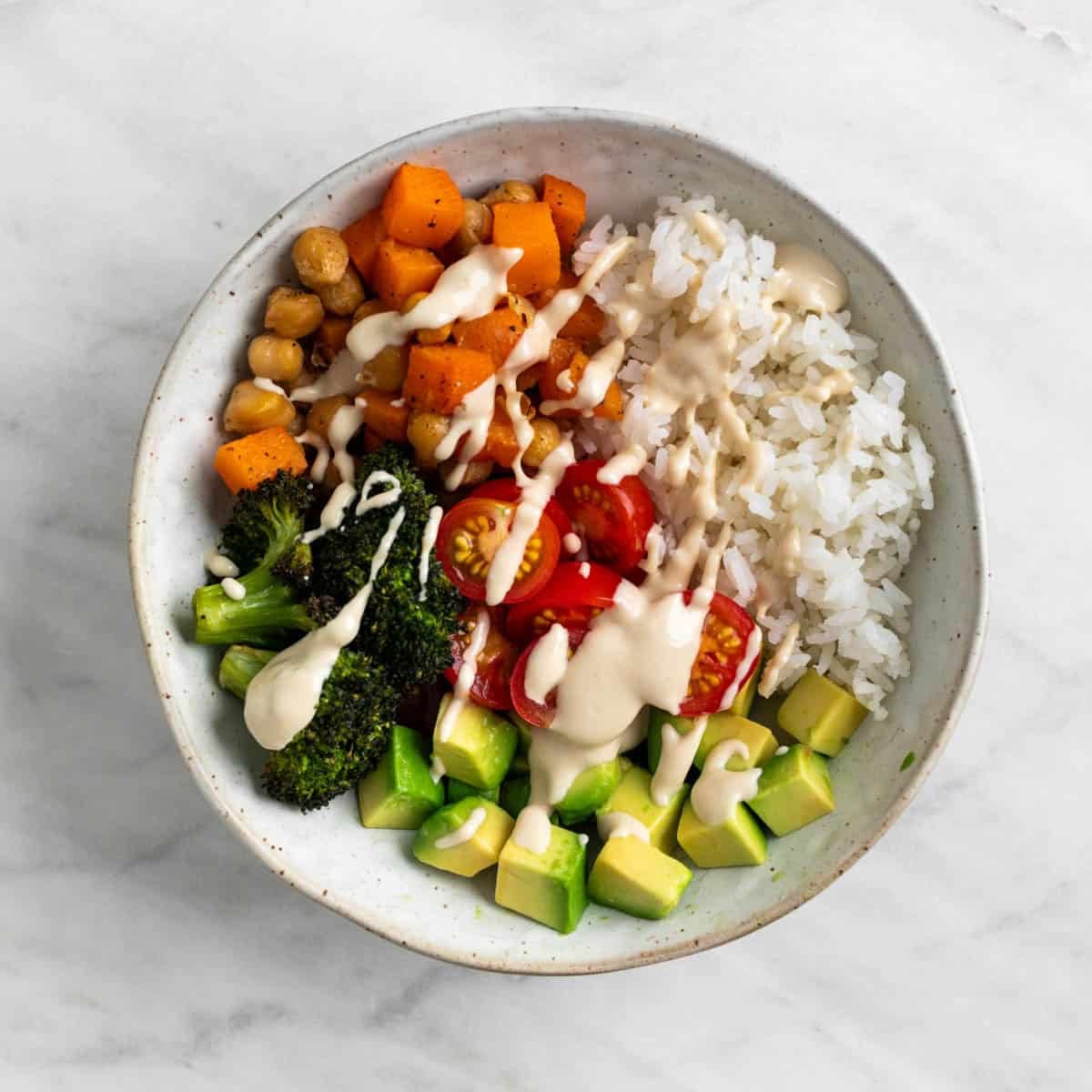 Vegan rice bowl with avocado, cherry tomatoes, and tahini dressing.