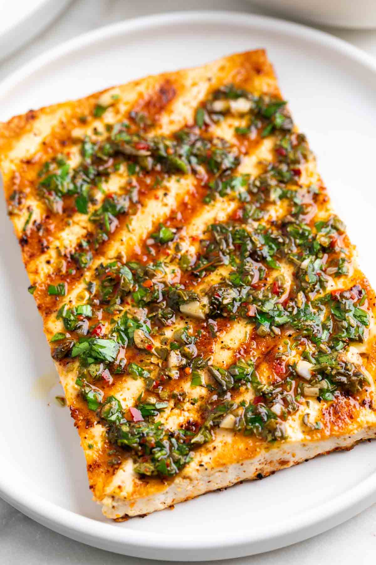 Grilled tofu steak on a plate topped with chimichurri.