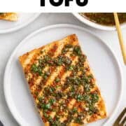 Two plates of grilled tofu with chimichurri, served with a fork and extra sauce.