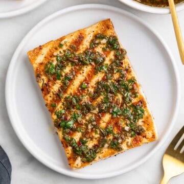 Two plates of grilled tofu steaks topped with chimichurri, with a fork and extra chimichurri around.