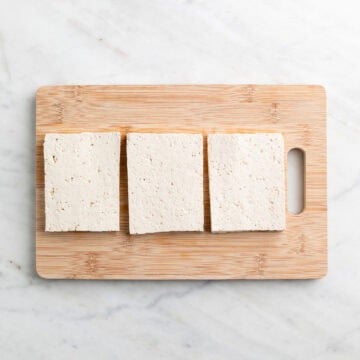 Block of tofu cut into three thick slabs on a cutting board.