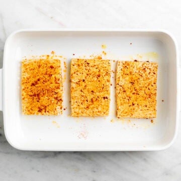 Tofu coated with a spice mixture using hands.