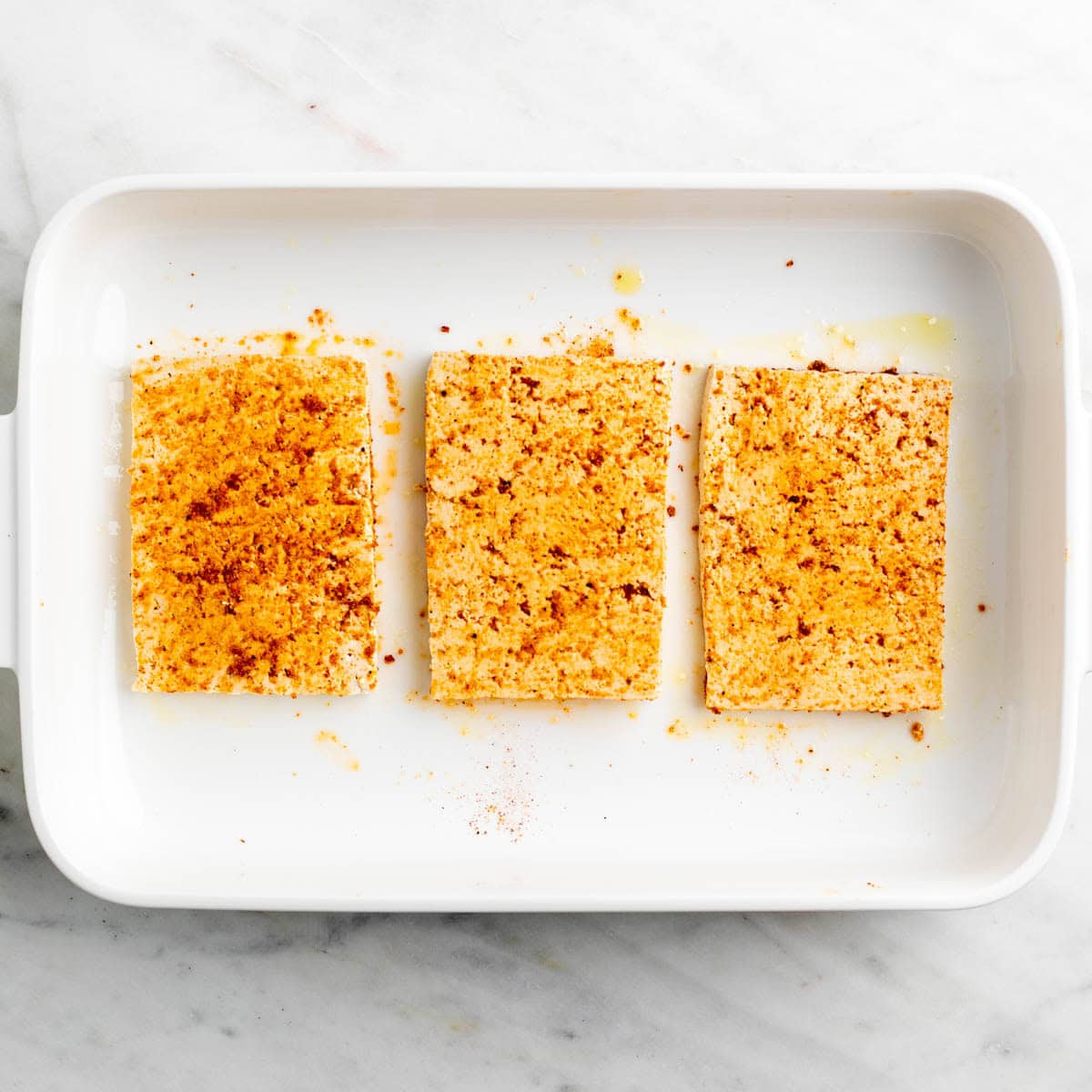 Tofu coated with a spice mixture using hands.