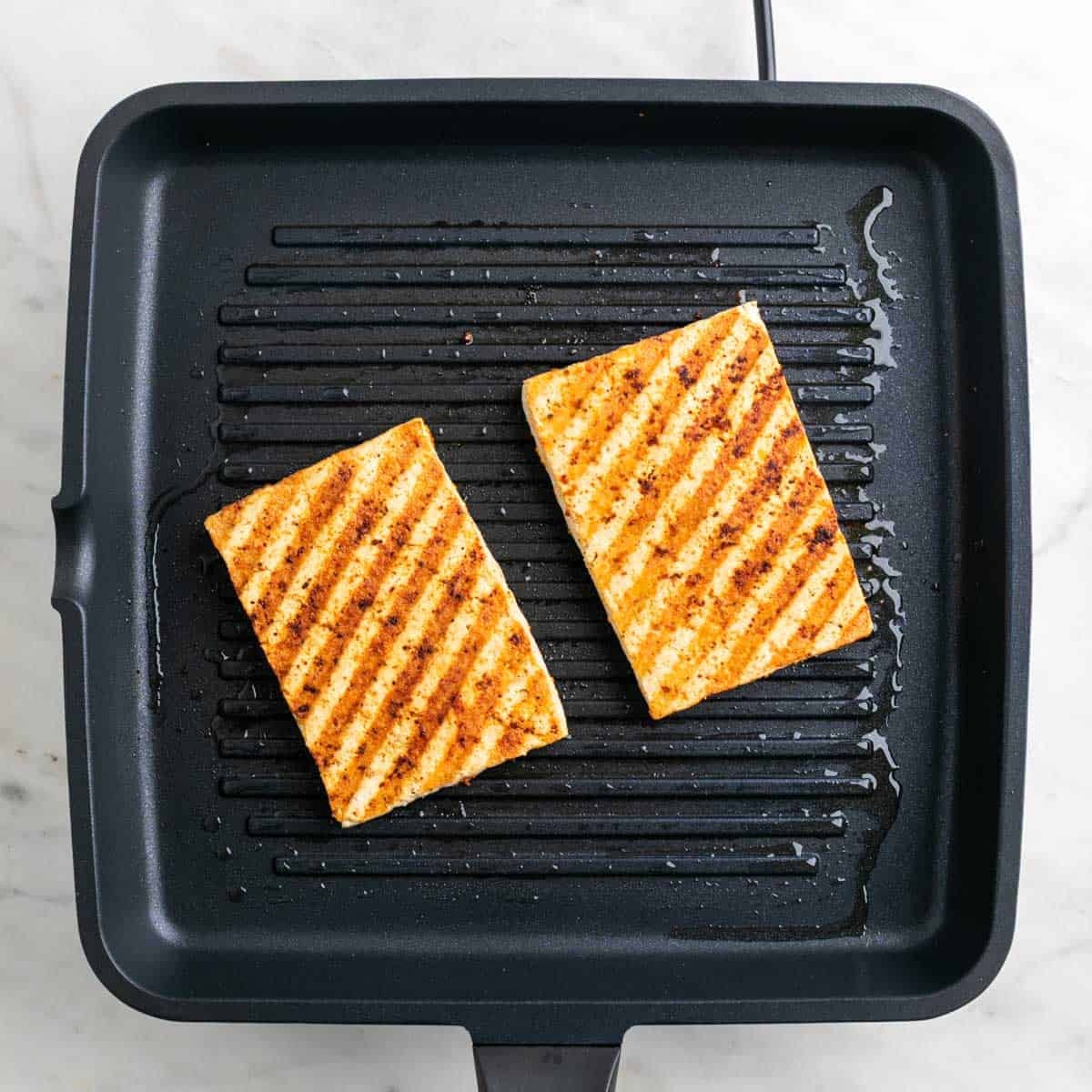 Tofu cooking on a grill pan with visible grill marks.
