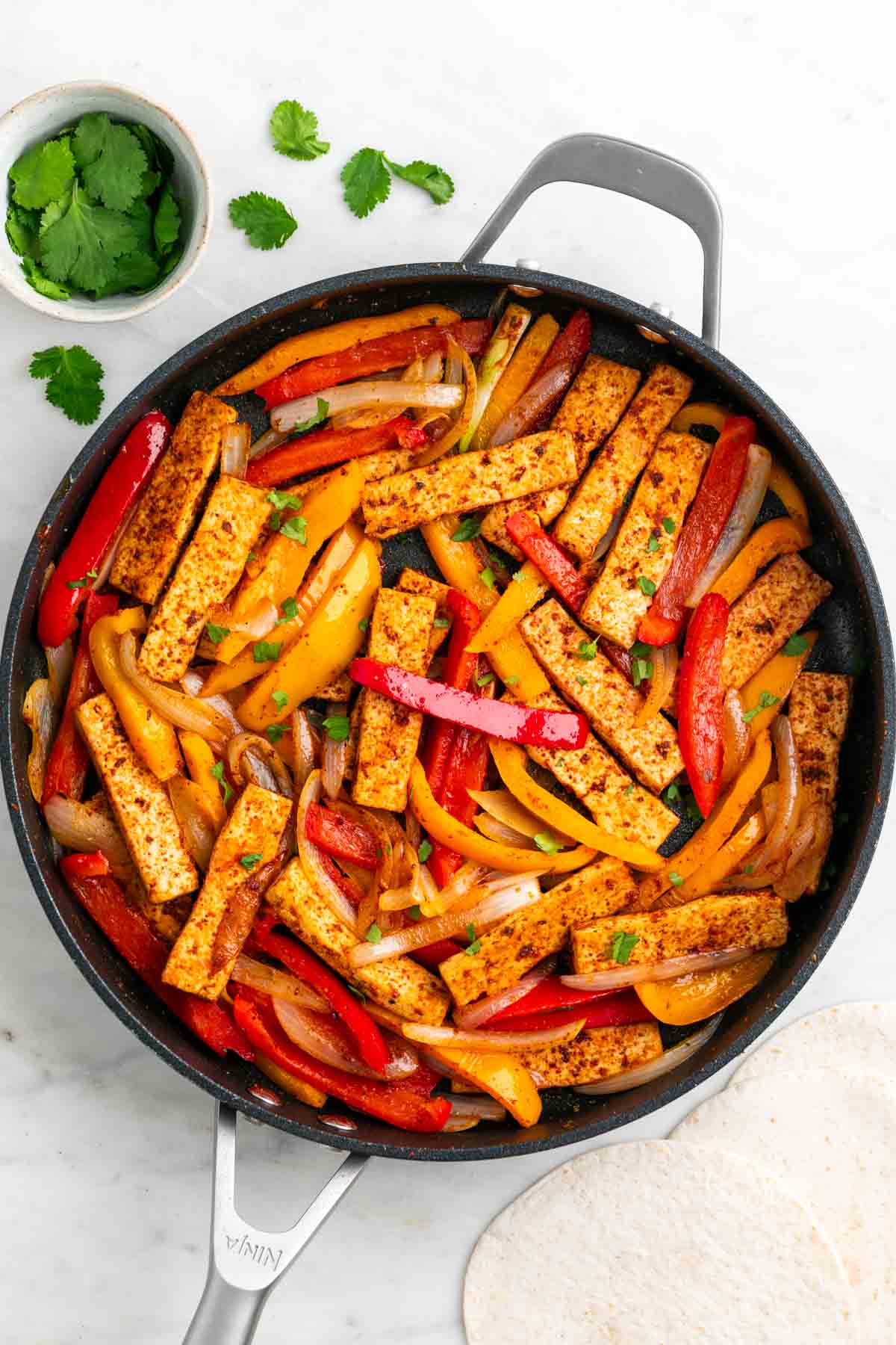 Tofu fajitas in a skillet topped with fresh cilantro