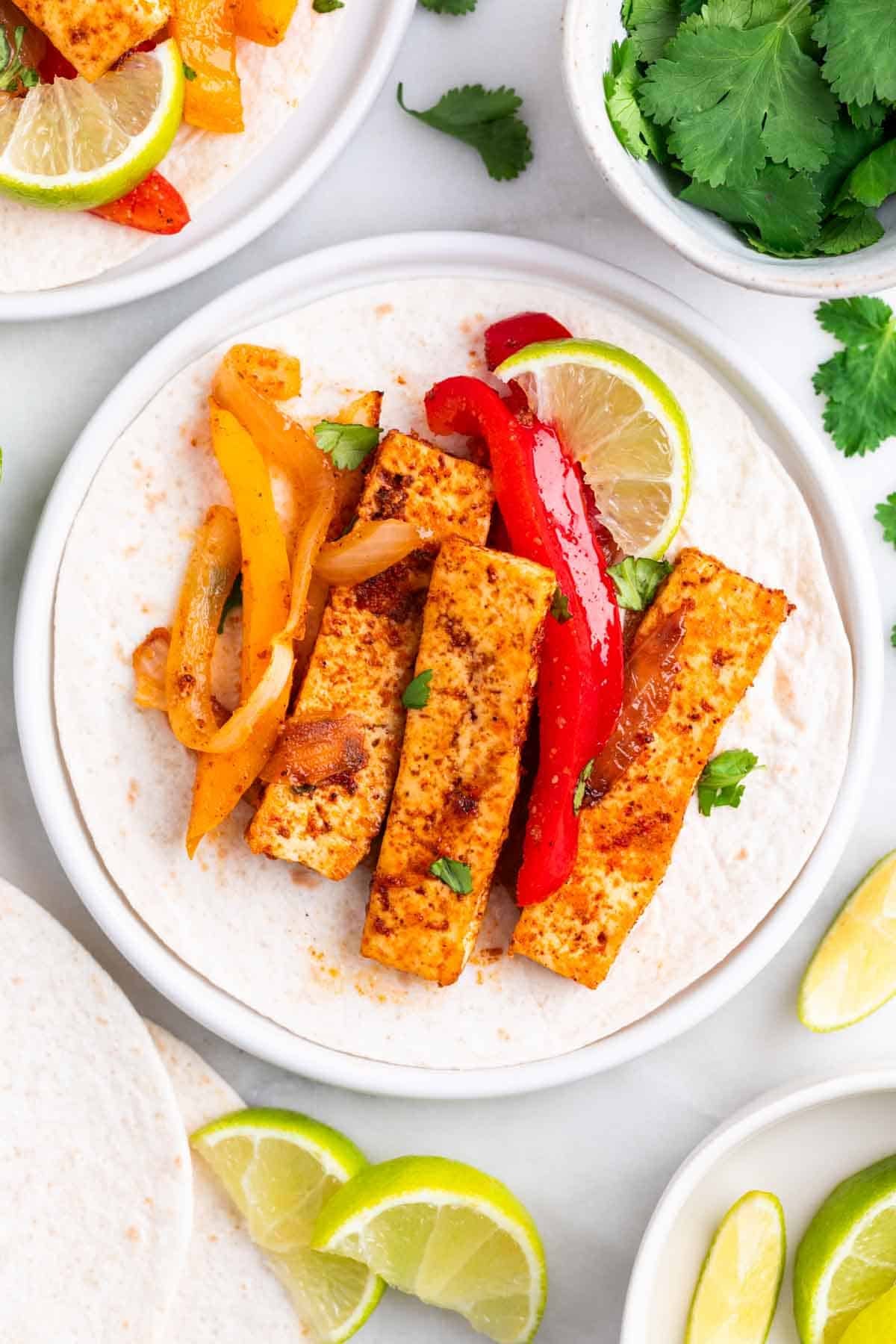 Tofu fajita filling on a tortilla with sliced lime