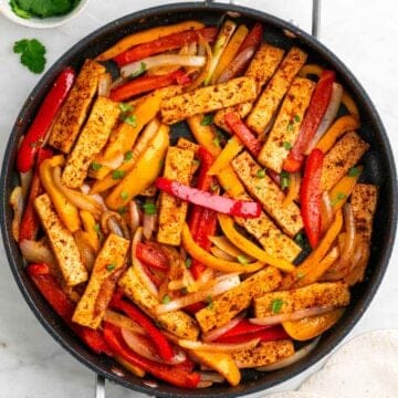 Tofu fajitas with peppers and onions topped with fresh cilantro in a skillet